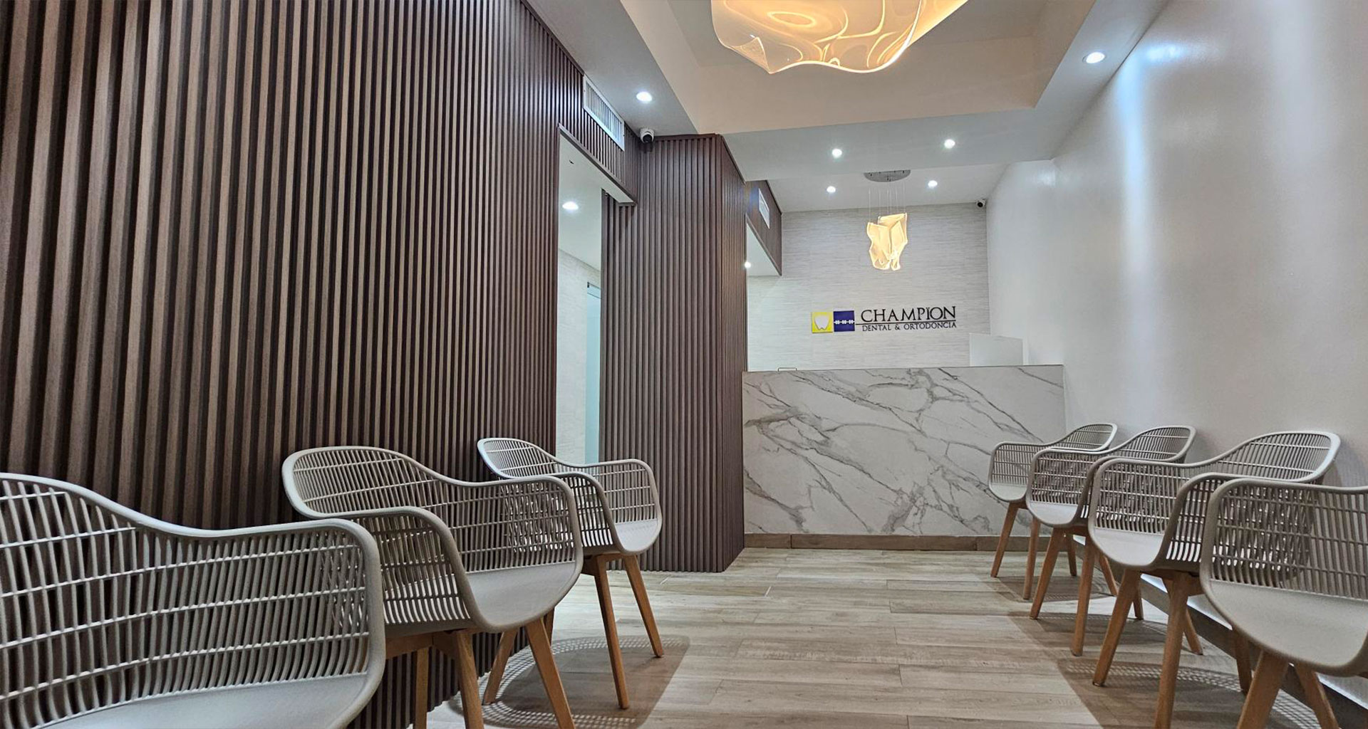 The image shows an interior space with a modern design, featuring a reception area with chairs and a counter, a wall with a geometric pattern, and a sign with the name  SACOM  visible.