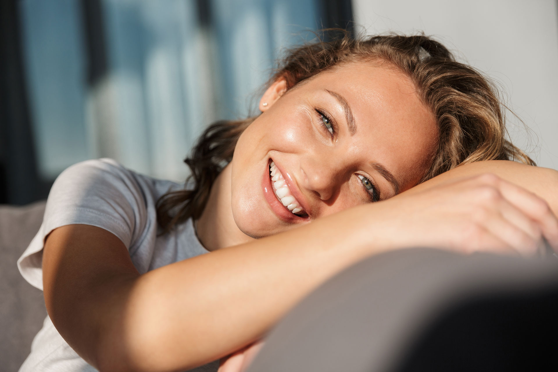 A woman with a radiant smile, resting her head on a couch cushion.