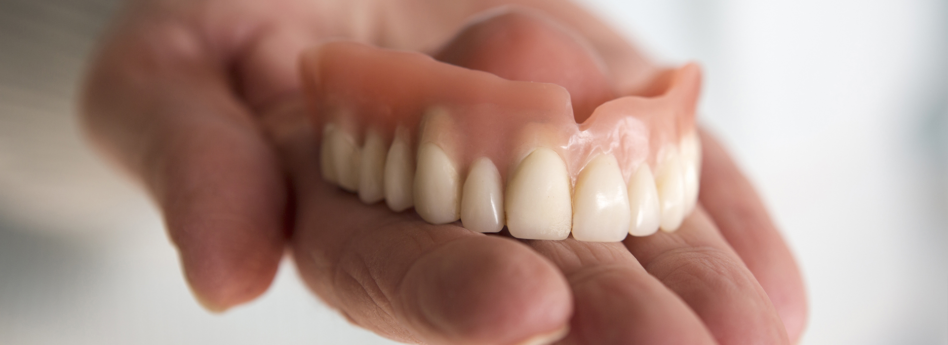 A person holding a set of dentures, showcasing the prosthetic teeth in an open hand.