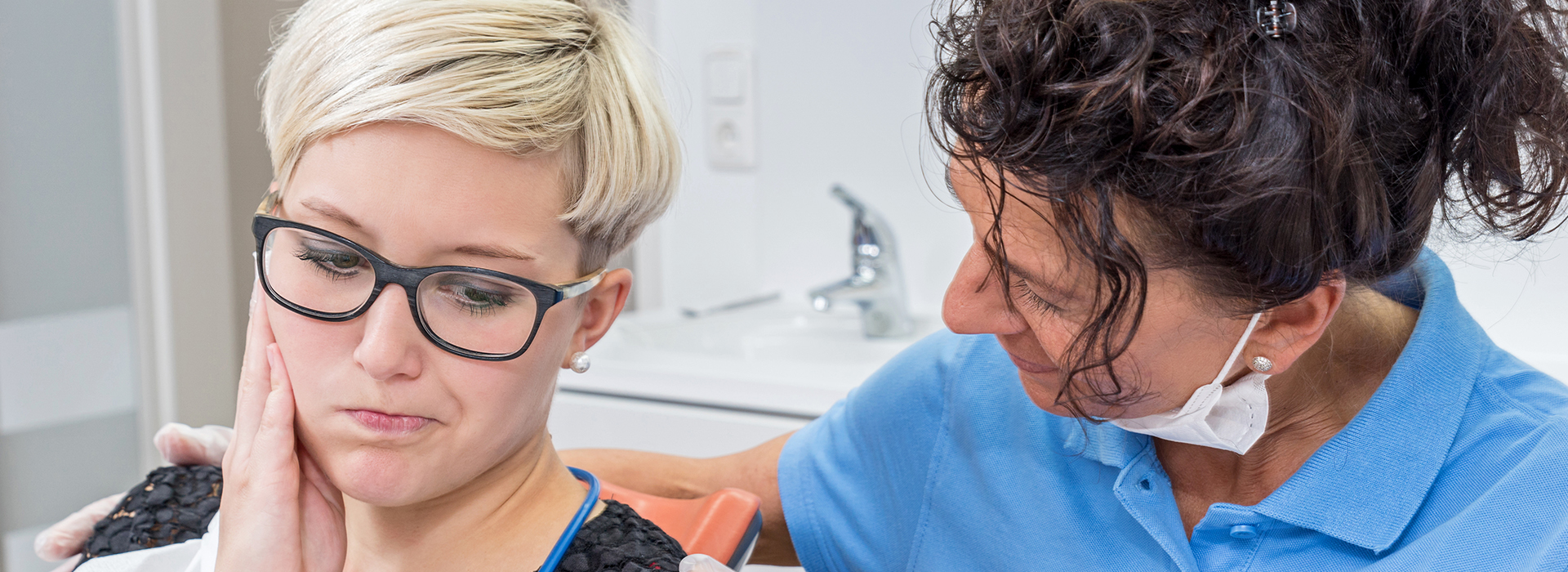 The image shows a person receiving dental care, likely a teeth cleaning or examination, from a dentist in a professional setting.