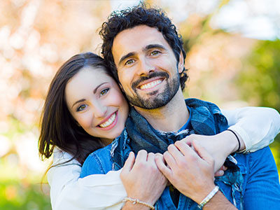 The image shows a man and a woman posing together, smiling and looking towards the camera.