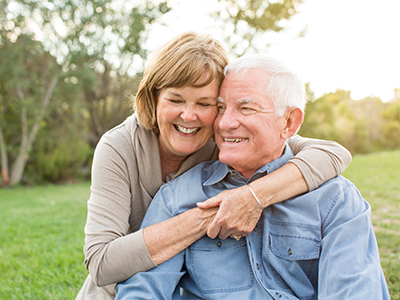 An elderly couple embracing in a park setting.