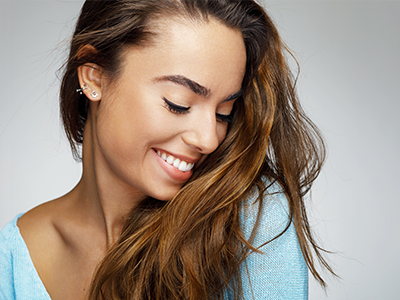 A young woman with long hair, wearing a light blue top, smiling gently and looking to her right.