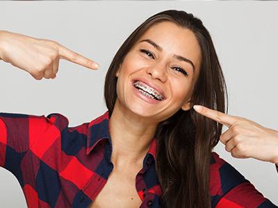 A woman with a toothy smile pointing to her teeth.