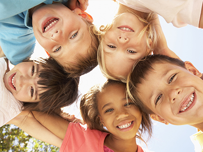 A group of children smiling and posing together in a sunny outdoor setting.