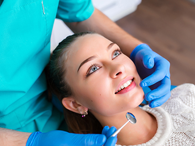 The image shows a woman sitting in a dental chair, receiving dental care from a professional wearing blue gloves and using dental tools.