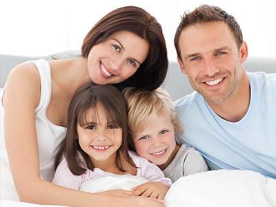 A family of four, including two adults and two children, posing together on a bed.