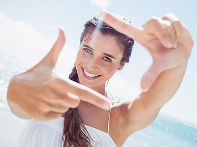 A woman is taking a selfie with her hand held up to the camera, smiling and looking directly at it.